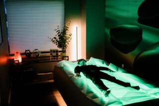 Person resting on a bed with green ambient lighting in a modern room.