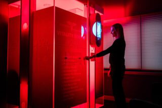 Woman standing by a red-lit vitality booth with a touchscreen interface.
